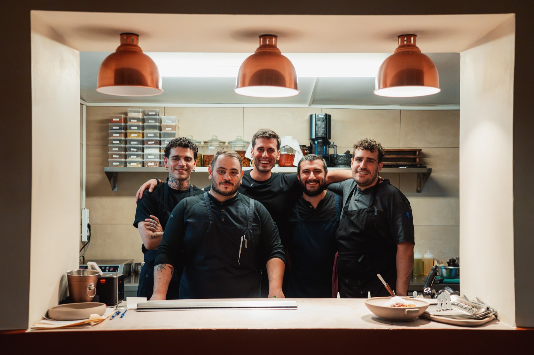 A kitchen team framed in the pass under copper lamps