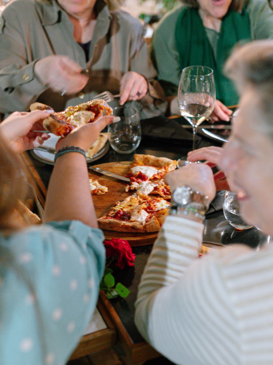 Friends sharing pizza and white wine around a table at Vissente